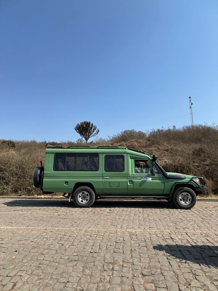 Green safari vehicle on a cobbled road in a dry landscape under clear skies.